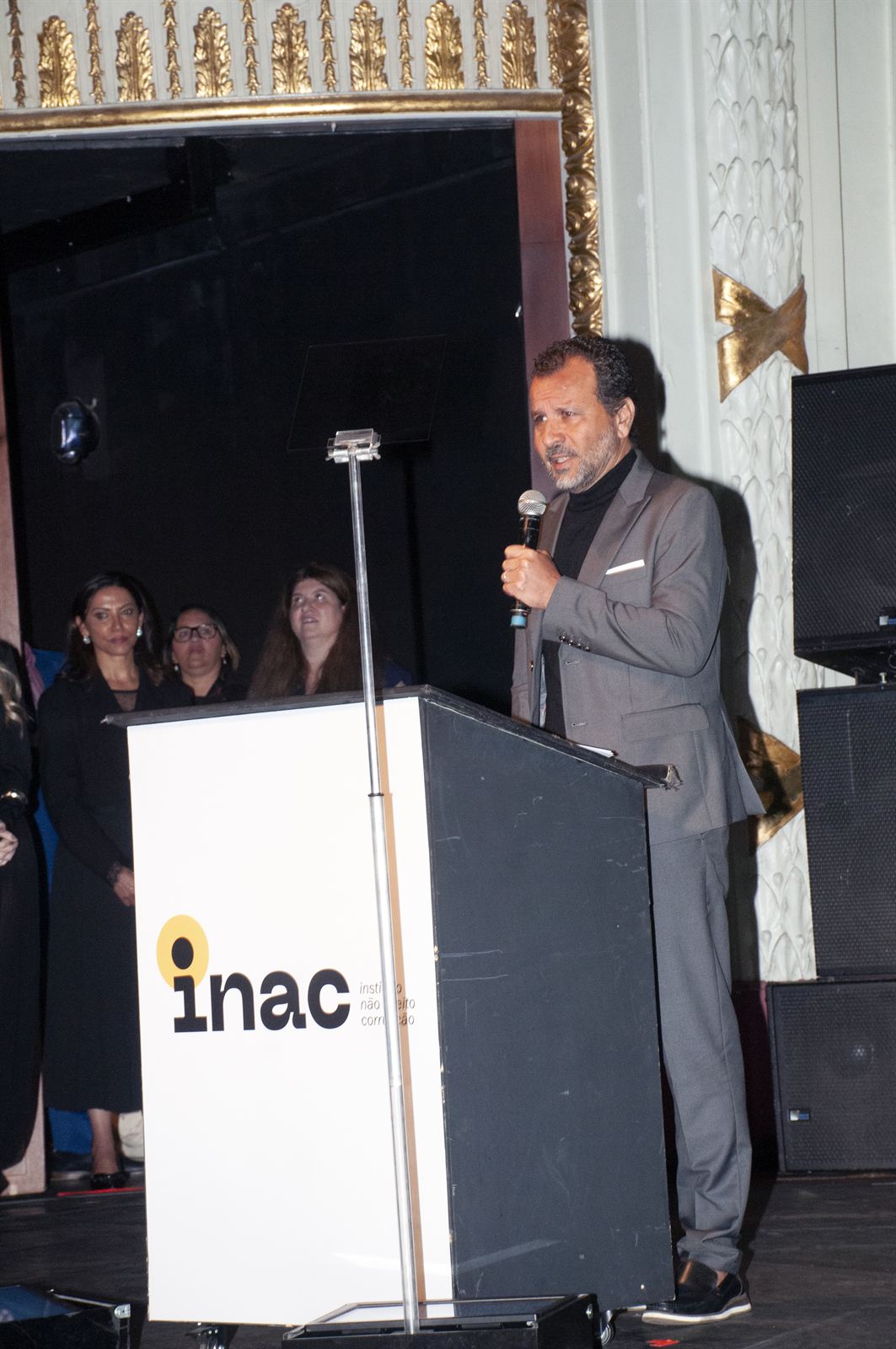 Márcio Medeiro Gomes discursando ao microfone no púlpito do INAC, no palco do Theatro Municipal de São Paulo